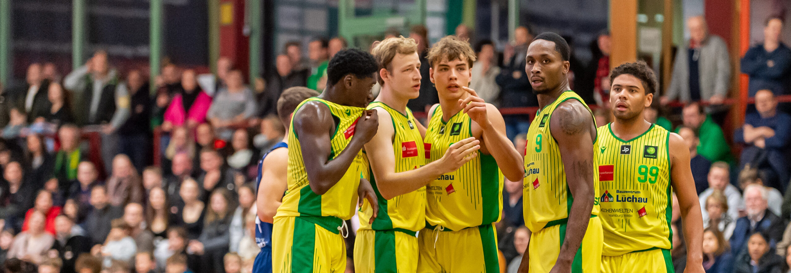 Basketballspieler in gelb-grünen Trikots mit der Aufschrift 'Licher' während eines Spiels in einer Halle mit Zuschauern