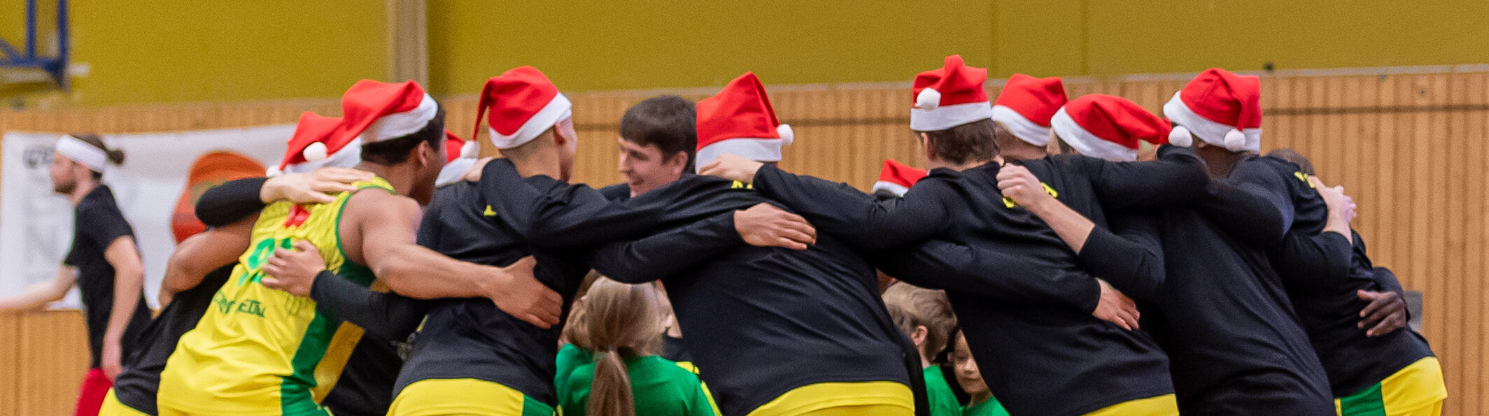 Sportler in Weihnachtsmützen umarmen sich im Kreis in einer Sporthalle