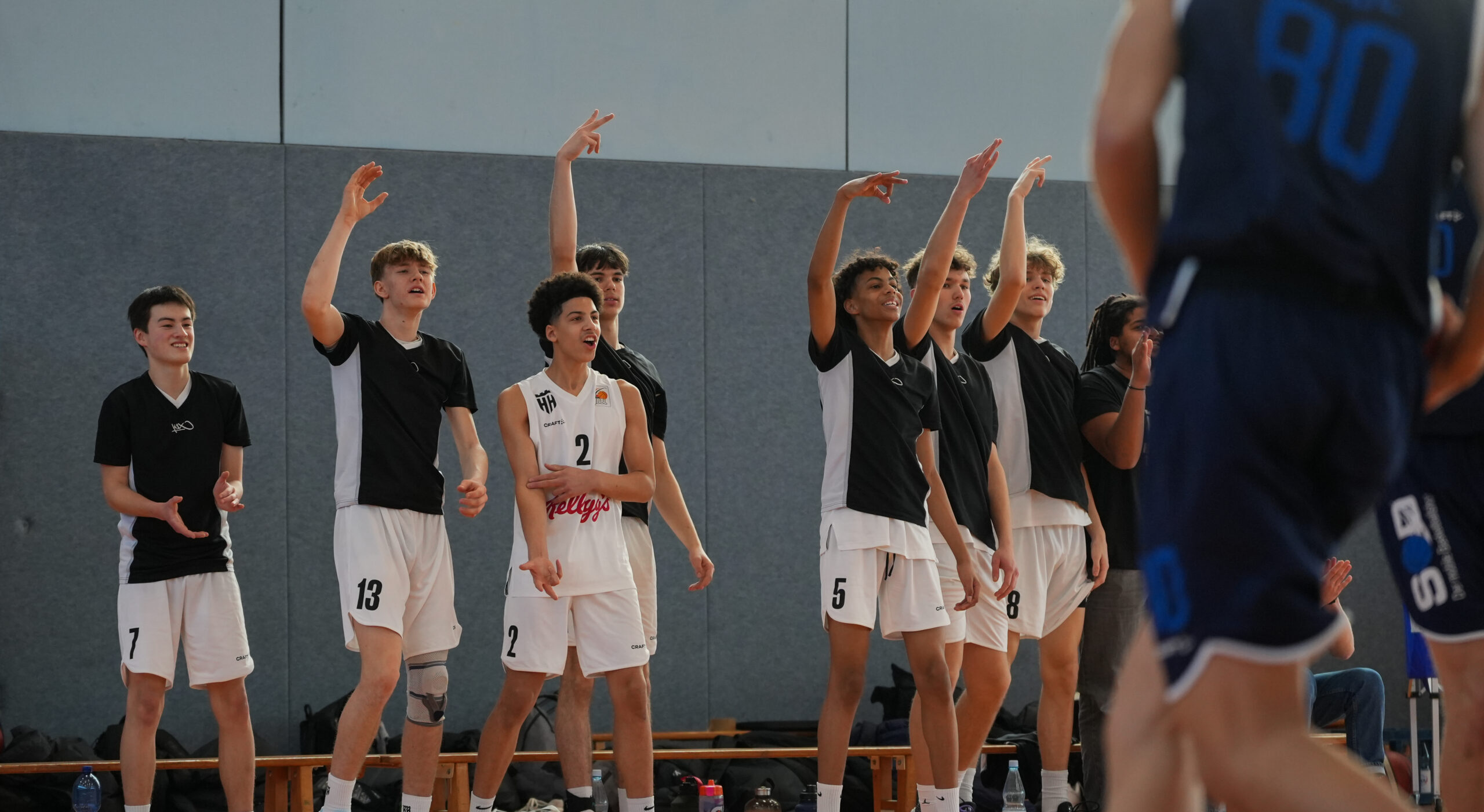 Junge Basketballspieler der Hamburg Towers in weißen Trikots stehen an der Seitenlinie und heben die Arme während eines Spiels