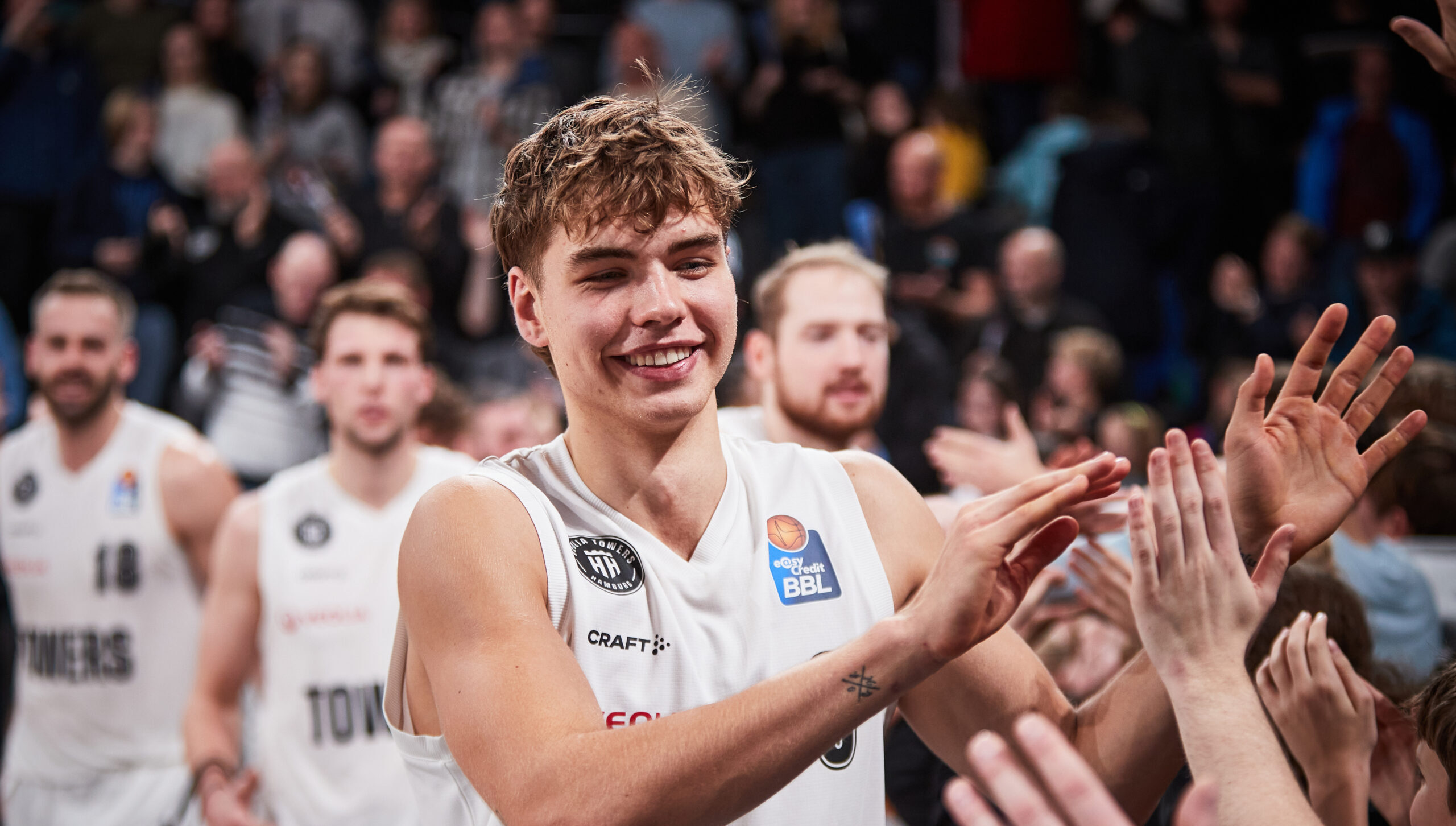 Leif Möller in weißem Trikot lächelt und klatscht bei wartenden Fans ab, im Hintergrund weitere Spieler