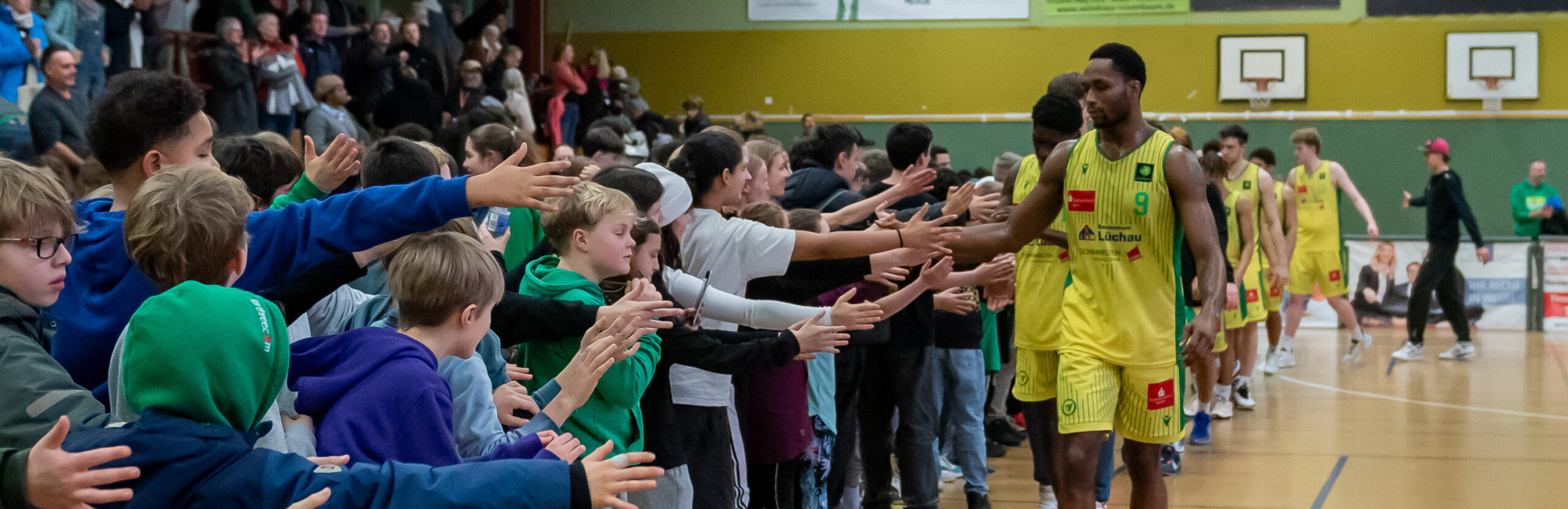 Basketballspieler in gelben Trikots geben Fans in der Halle High-Fives nach einem Spiel