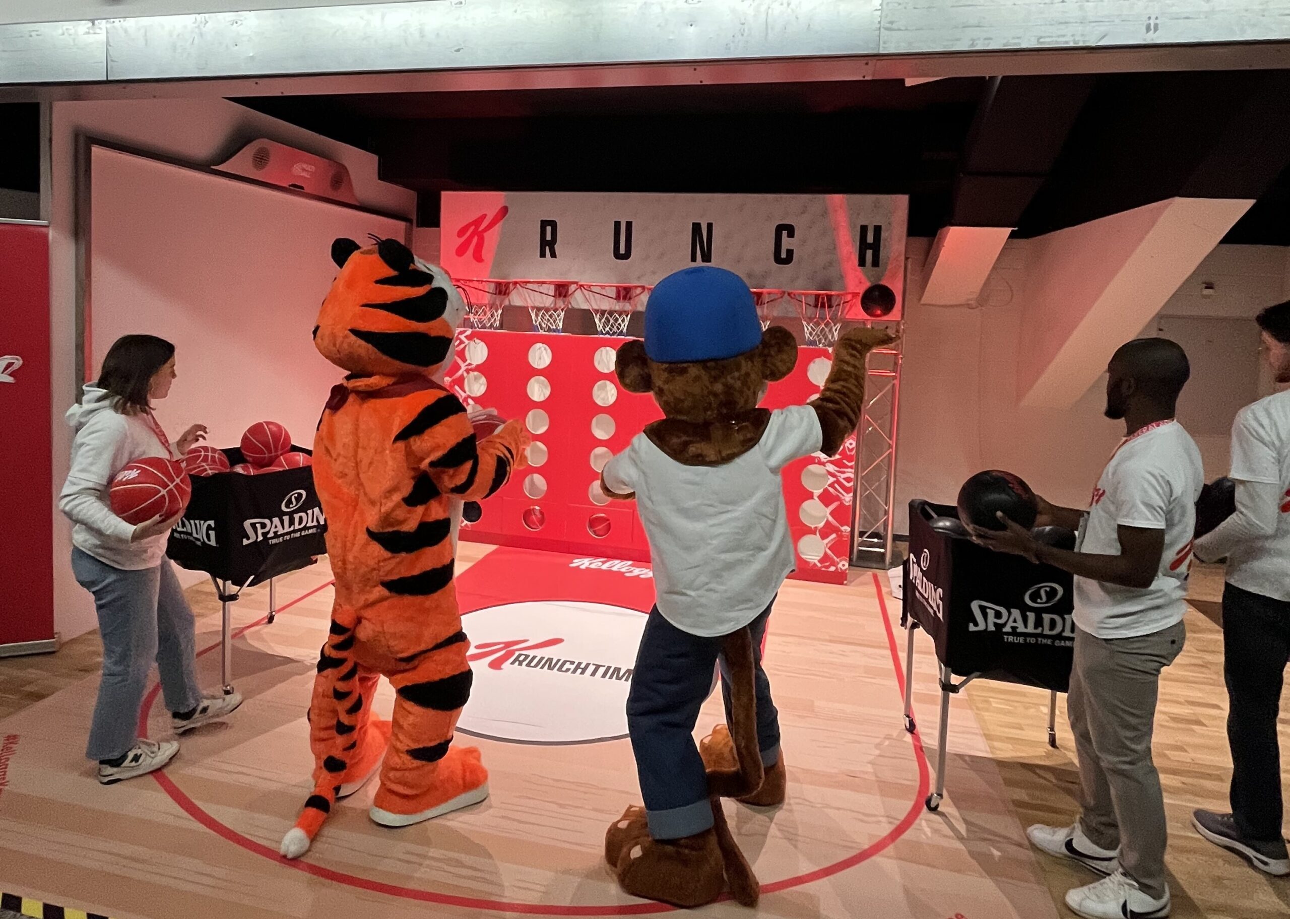 Menschen und Maskottchen spielen Basketball-Wurfspiel vor einer Kellogg's Crunch-Werbewand mit Spalding-Basketbällen