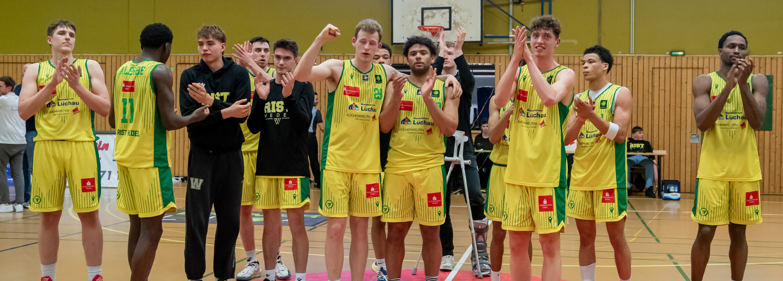 Basketballspieler in gelben Trikots stehen nebeneinander in einer Sporthalle und klatschen