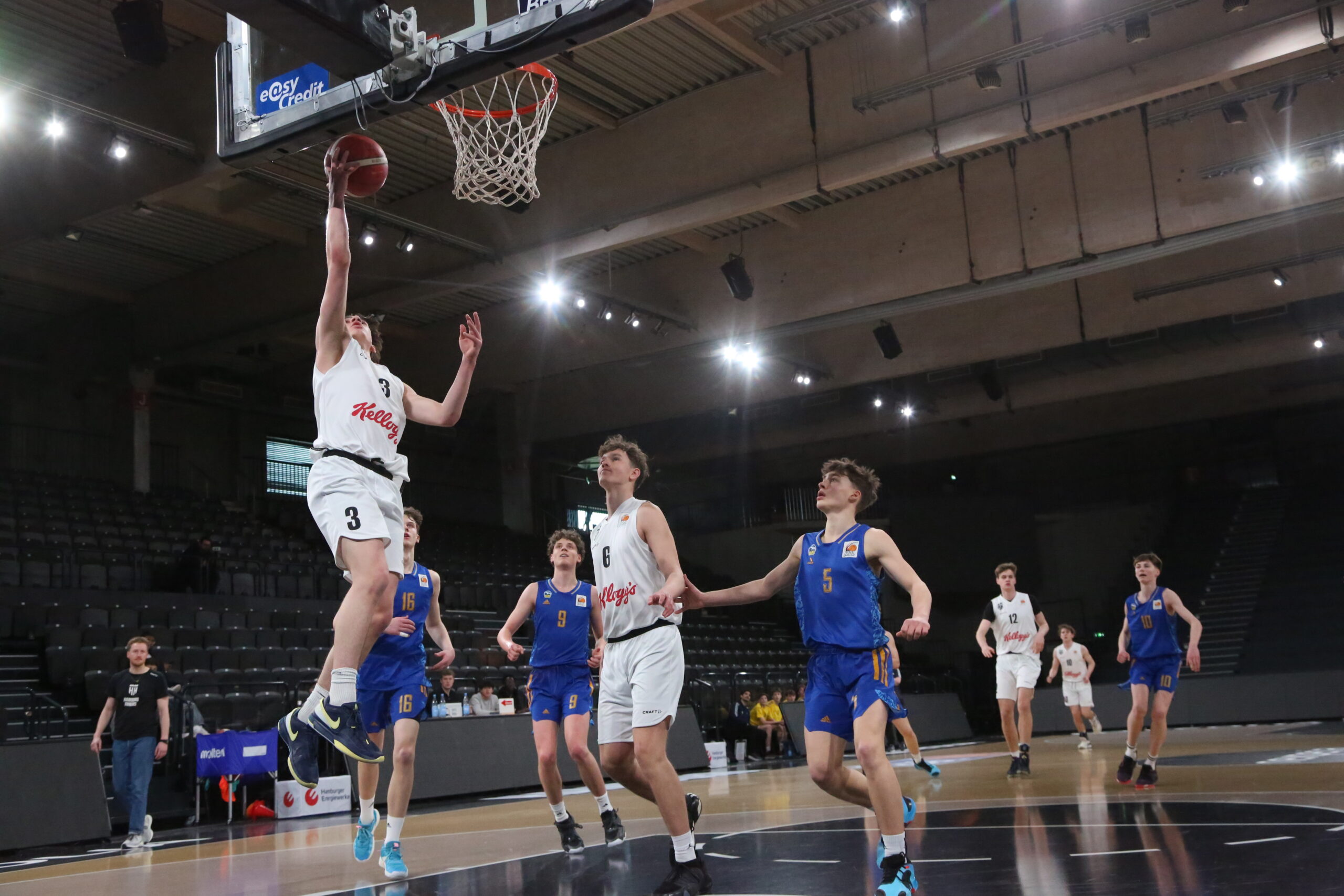 Junger Basketballspieler in weißer Trikotnummer wirft Ball, verteidigt von Spieler in blauem Trikot, Spiel Hamburg Towers gegen Alba Berlin