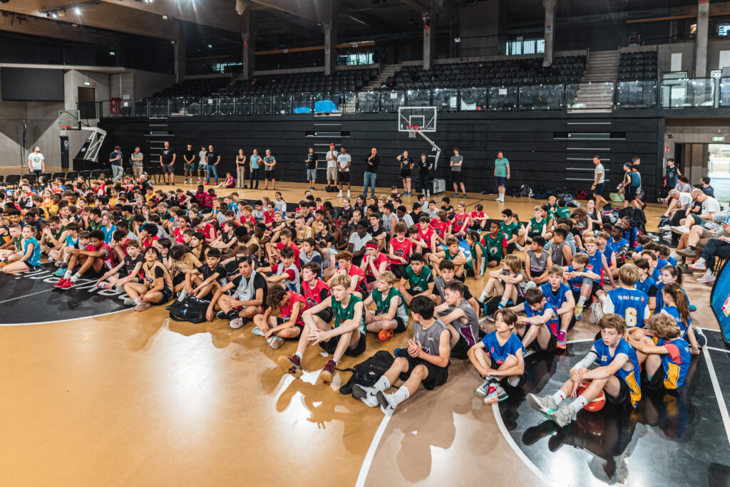 Kinder der Jr.NBA sitzen aufgereiht auf dem Feld der Inselpark Arena