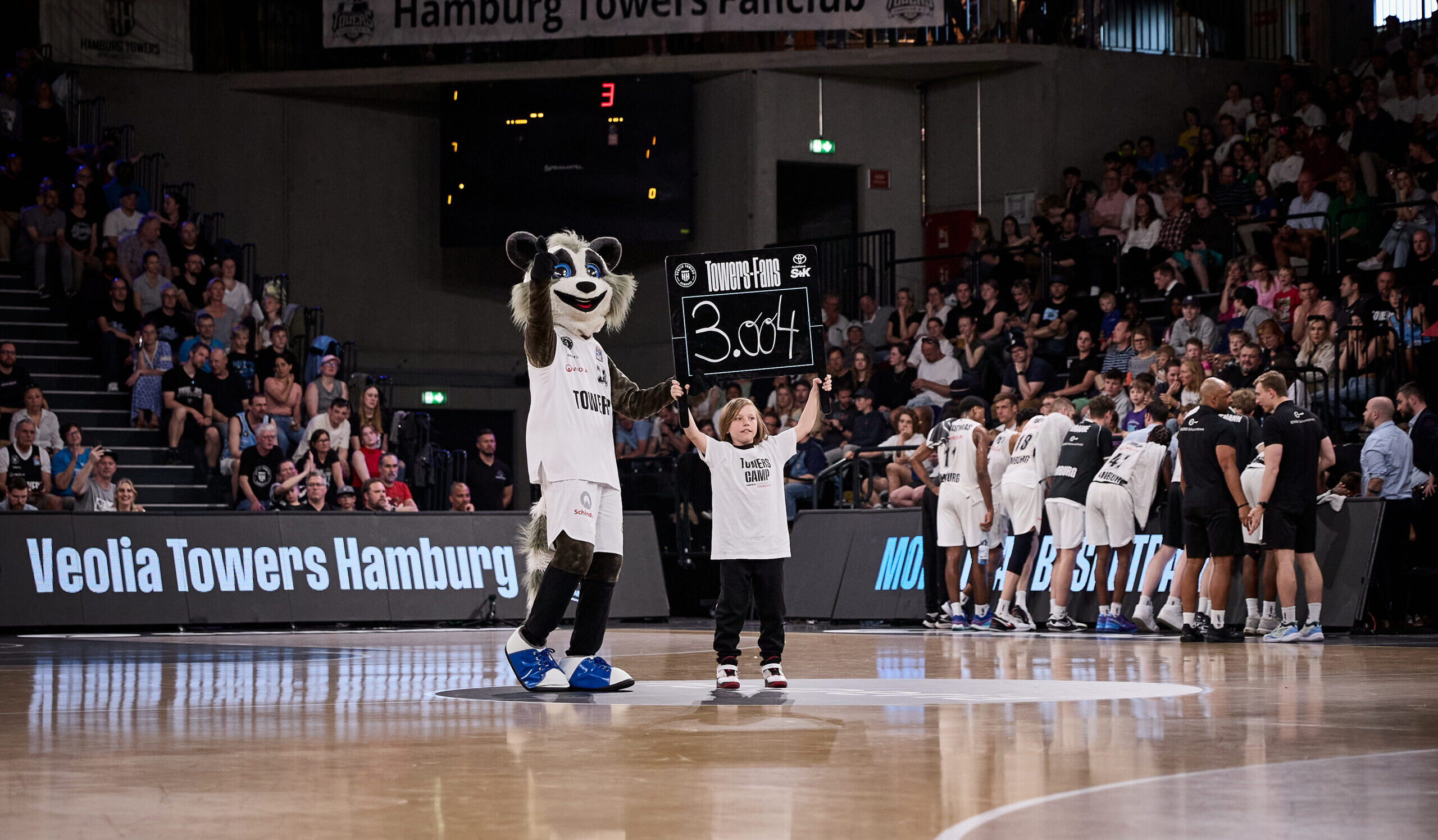Tipoff-Kind präsentiert mit Maskottchen Willy die Zuschauerzahl auf einem Schild