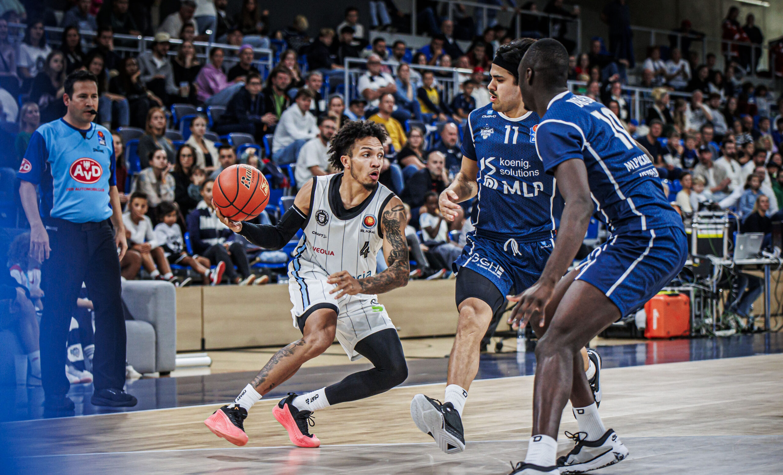 Jaizec Lottie dribbelt den Ball, wird von Spielern in blauen Uniformen verteidigt