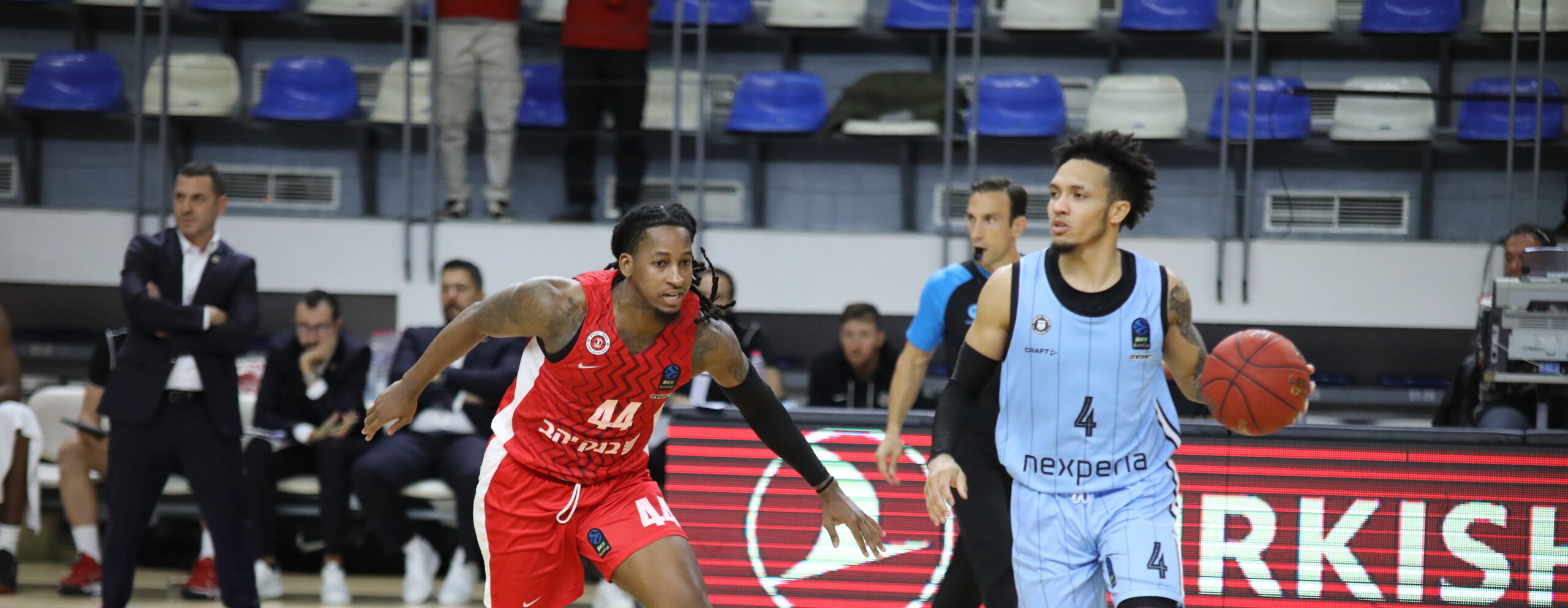 Basketballspieler in rotem Trikot mit der Nummer 44 verteidigt gegen Spieler in hellblauem Trikot mit der Nummer 4, der den Ball dribbelt