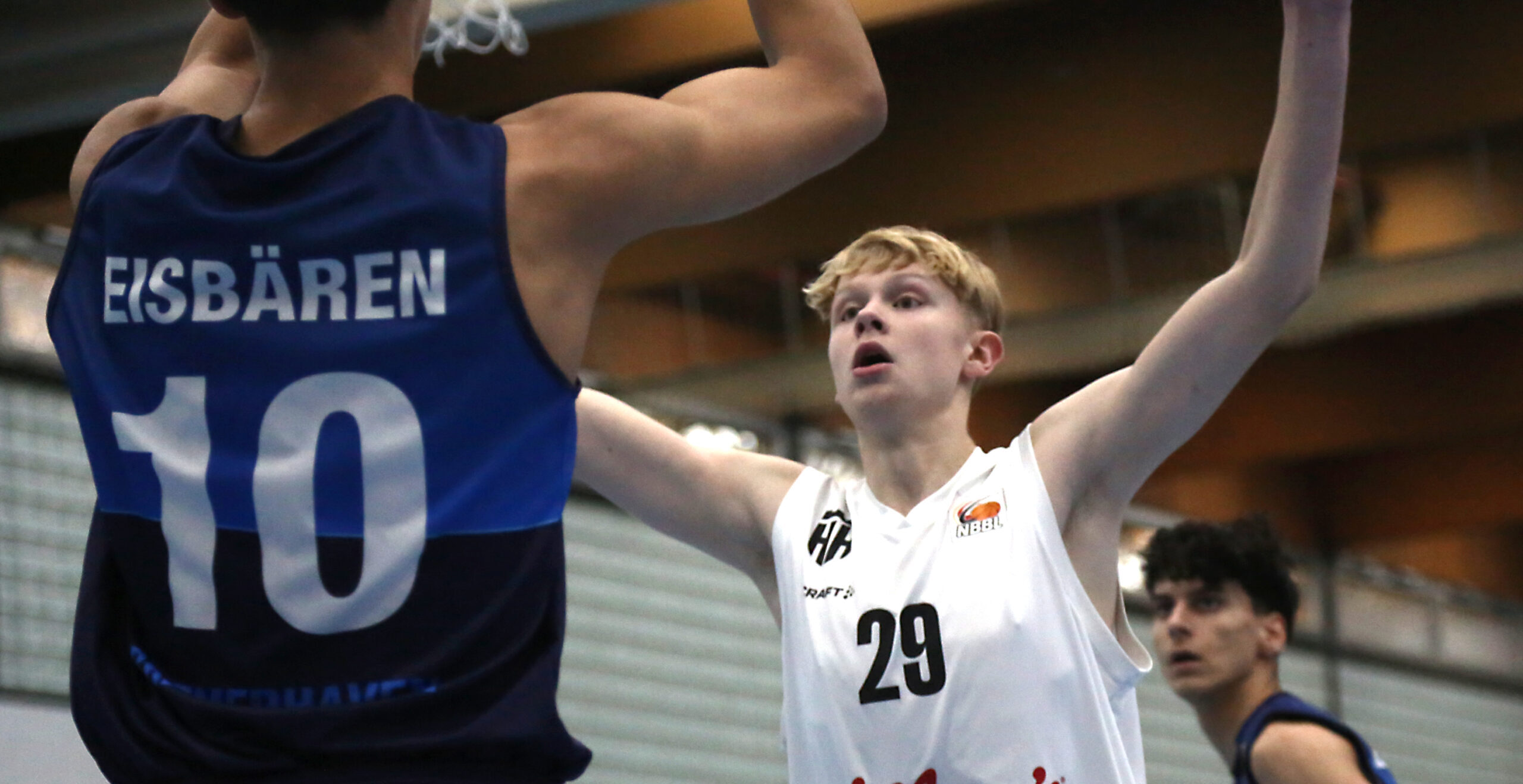 Zwei Basketballspieler in Aktion, einer trägt blaues Trikot mit Nummer 10 und Schriftzug 'Eisbären', der andere weißes Trikot mit Nummer 29, Arme erhoben
