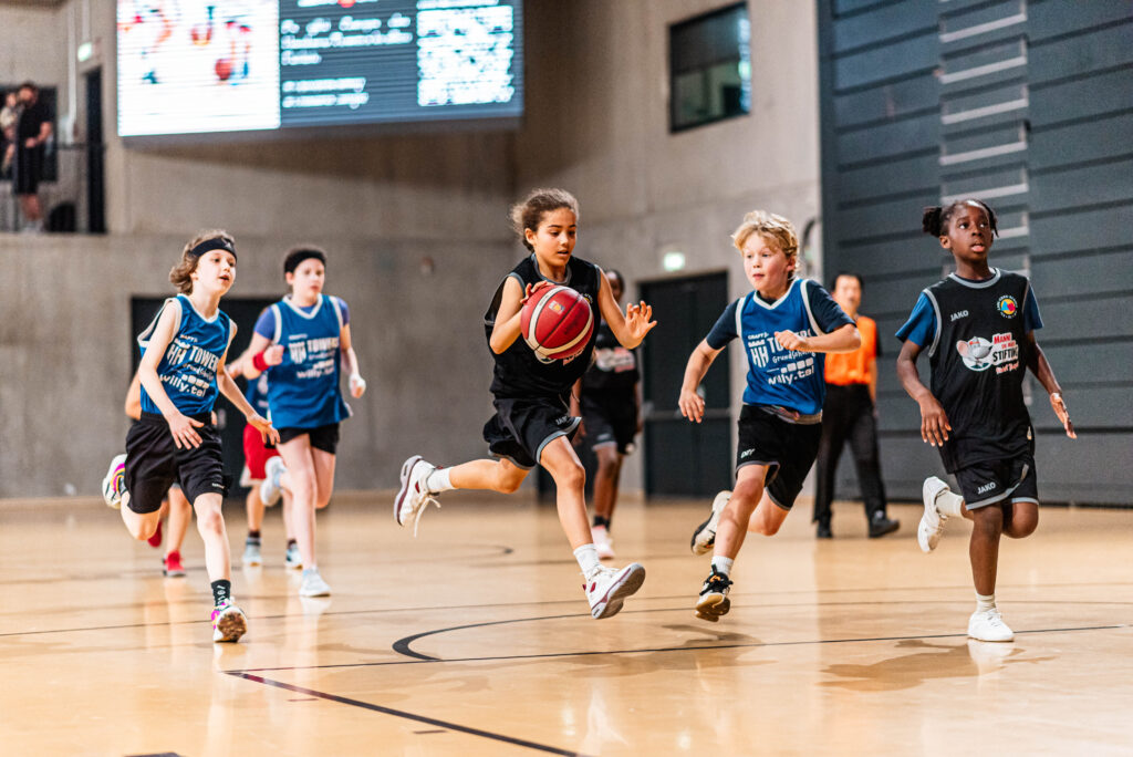 Fünf Kinder spielen Basketball in einer Halle