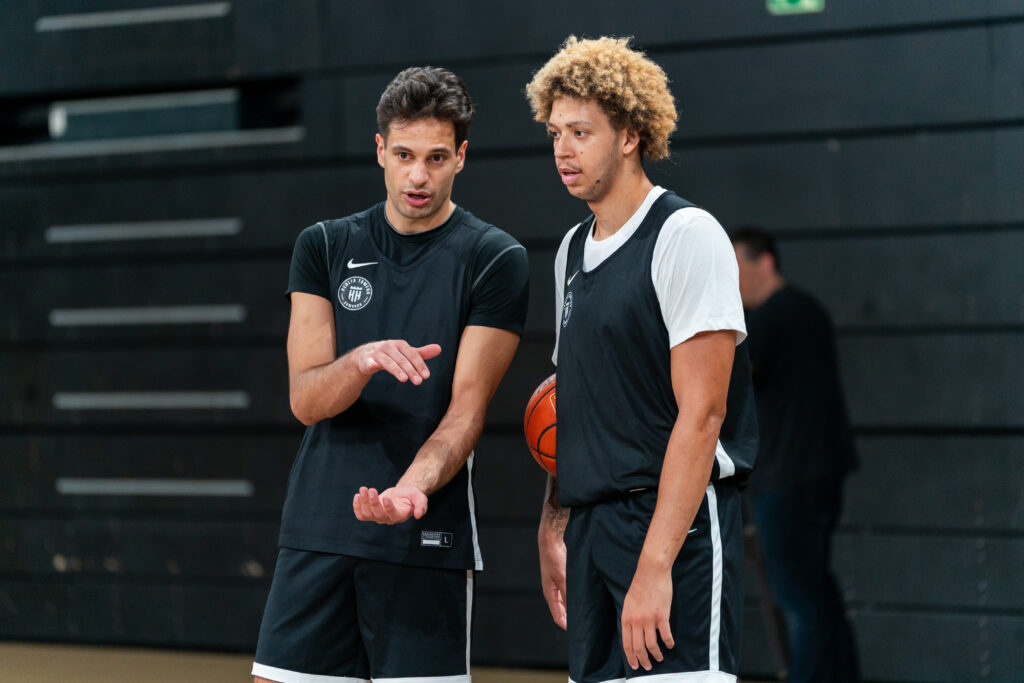Zwei Basketballspieler in schwarzen Trikots und Hosen im Gespräch miteinander