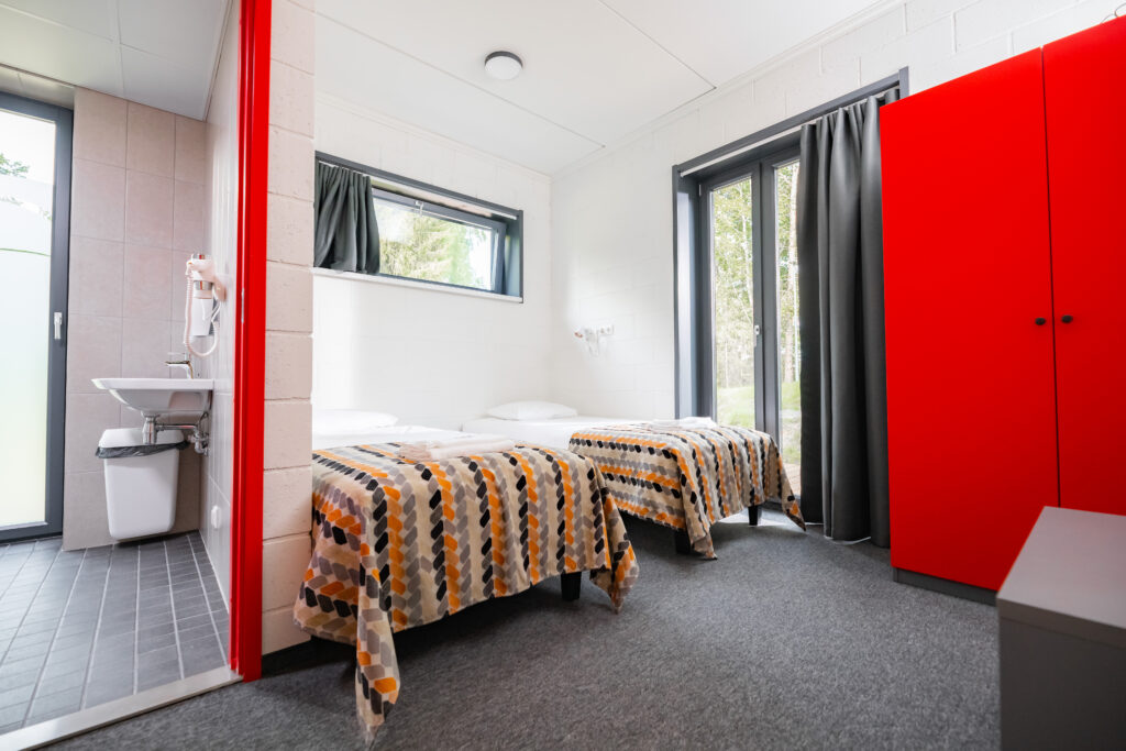 zwei Bette in einem Zimmer mit einem roten Schrank und geöffneter Badtür