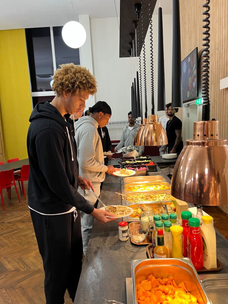 Mann in schwarzem Trainingsanzug steht an einem Buffett