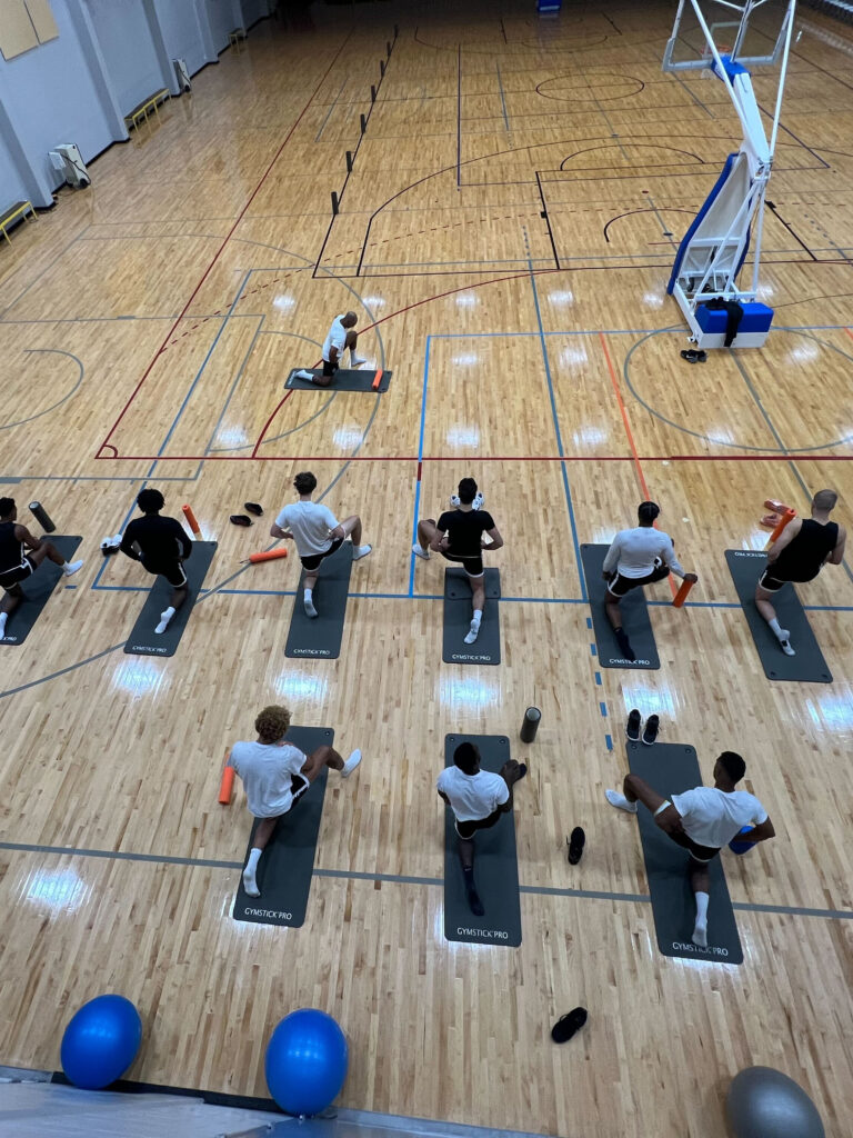 12 Sportler stretchen sich in einer Halle