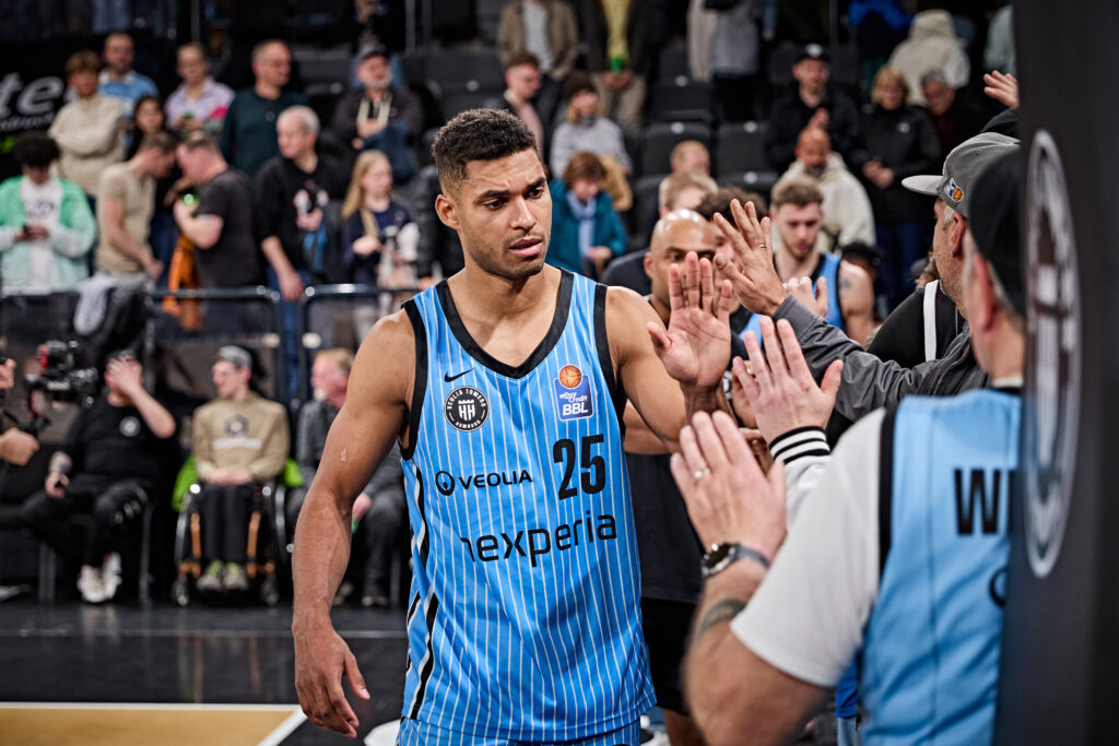 Basketballspieler in blau-schwarzem Trikot mit der Nummer 25 gibt Fans am Spielfeldrand High-Fives.