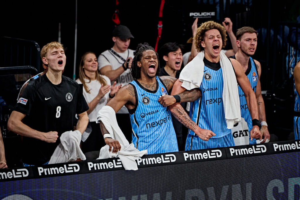 Mehrere Basketballspieler in blauen Trikots mit Aufschrift 'nexpe' und weißen Handtüchern stehen an der Bande mit Werbung 'PrimeLED'.