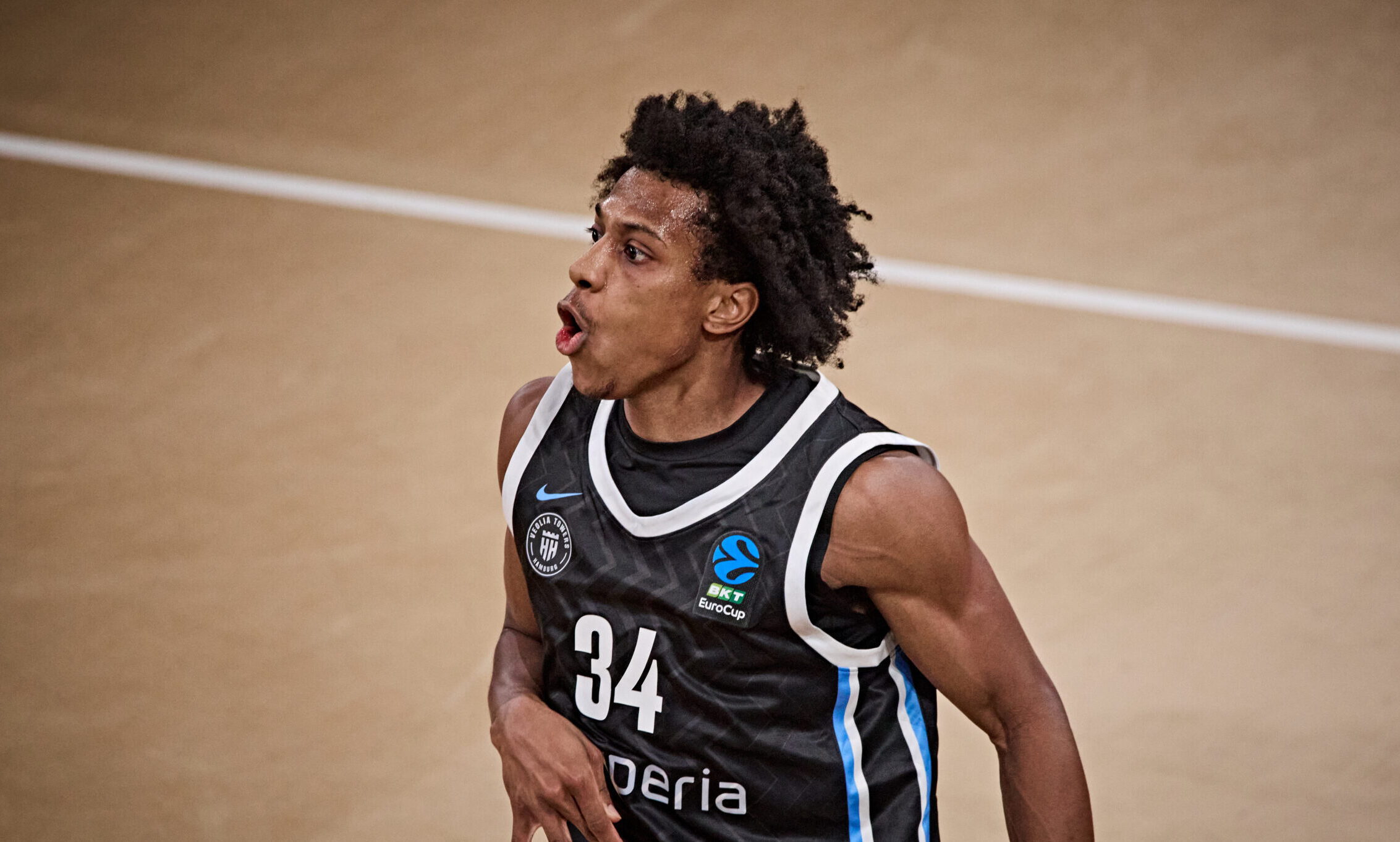 Basketballspieler mit Trikotnummer 34 in schwarzem Trikot mit weißen und blauen Streifen auf dem Spielfeld
