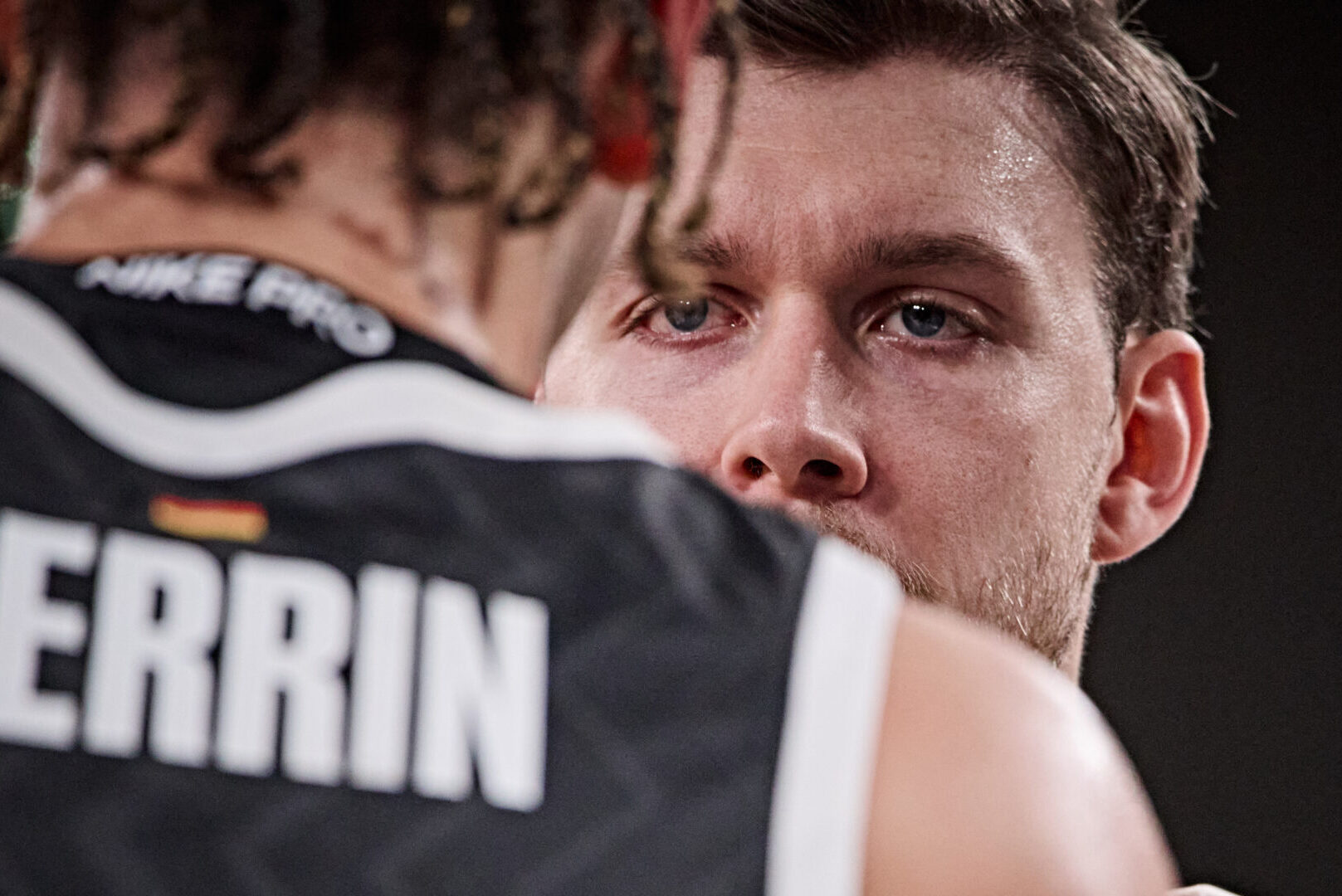 Zwei Basketballspieler in schwarzen Trikots mit den Aufschriften 'PERRIN' und 'VEOLIA' auf der Rückseite, einer mit sichtbarem Arm-Tattoo