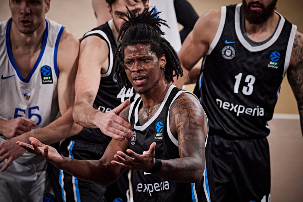 Mehrere Basketballspieler in Aktion, zwei tragen schwarze Trikots mit der Aufschrift 'nexperia', einer ein weißes Trikot mit der Nummer 55.