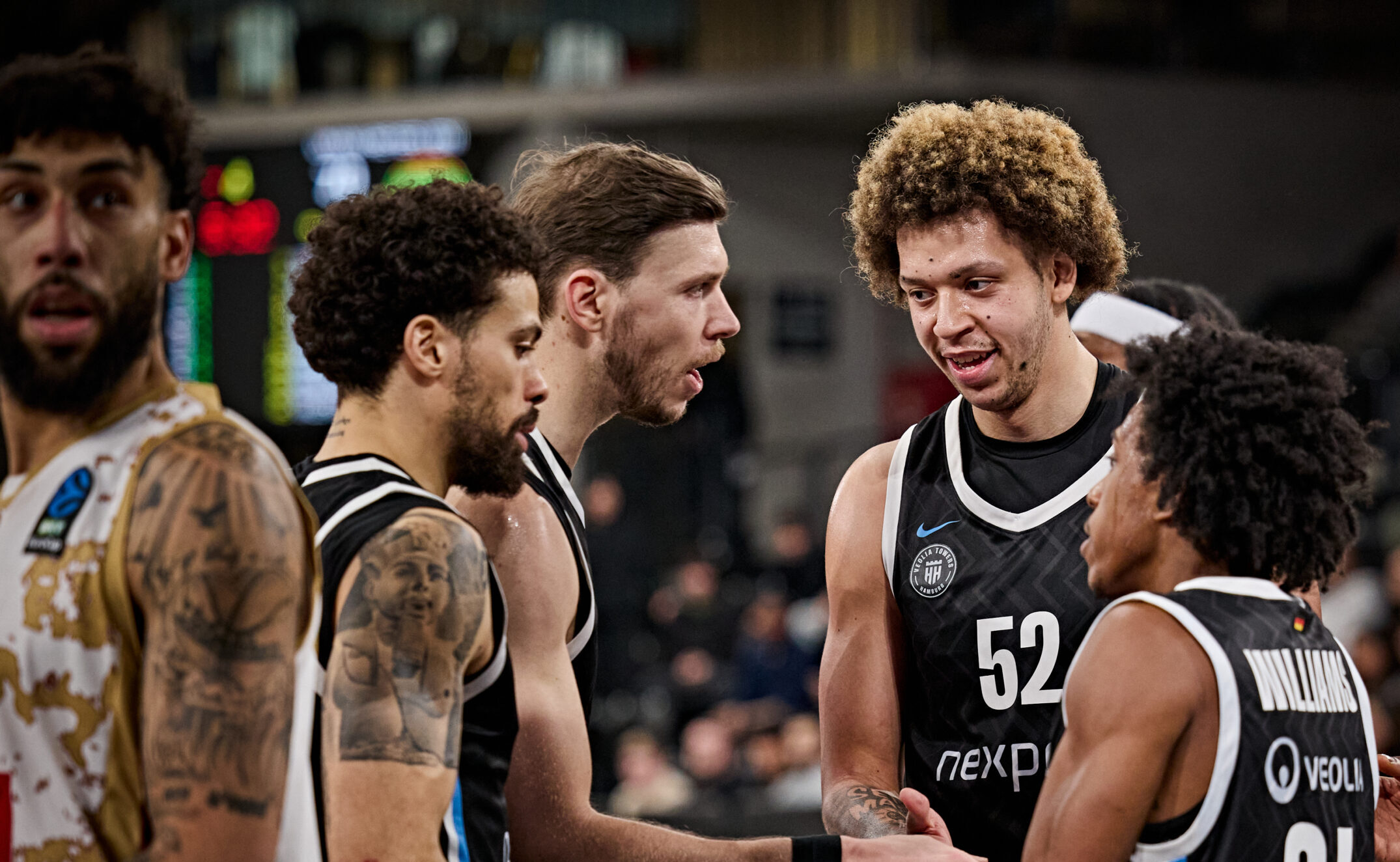 Basketballspieler in schwarzen Trikots mit den Nummern 52 und 34 geben sich die Hand in einer Sporthalle