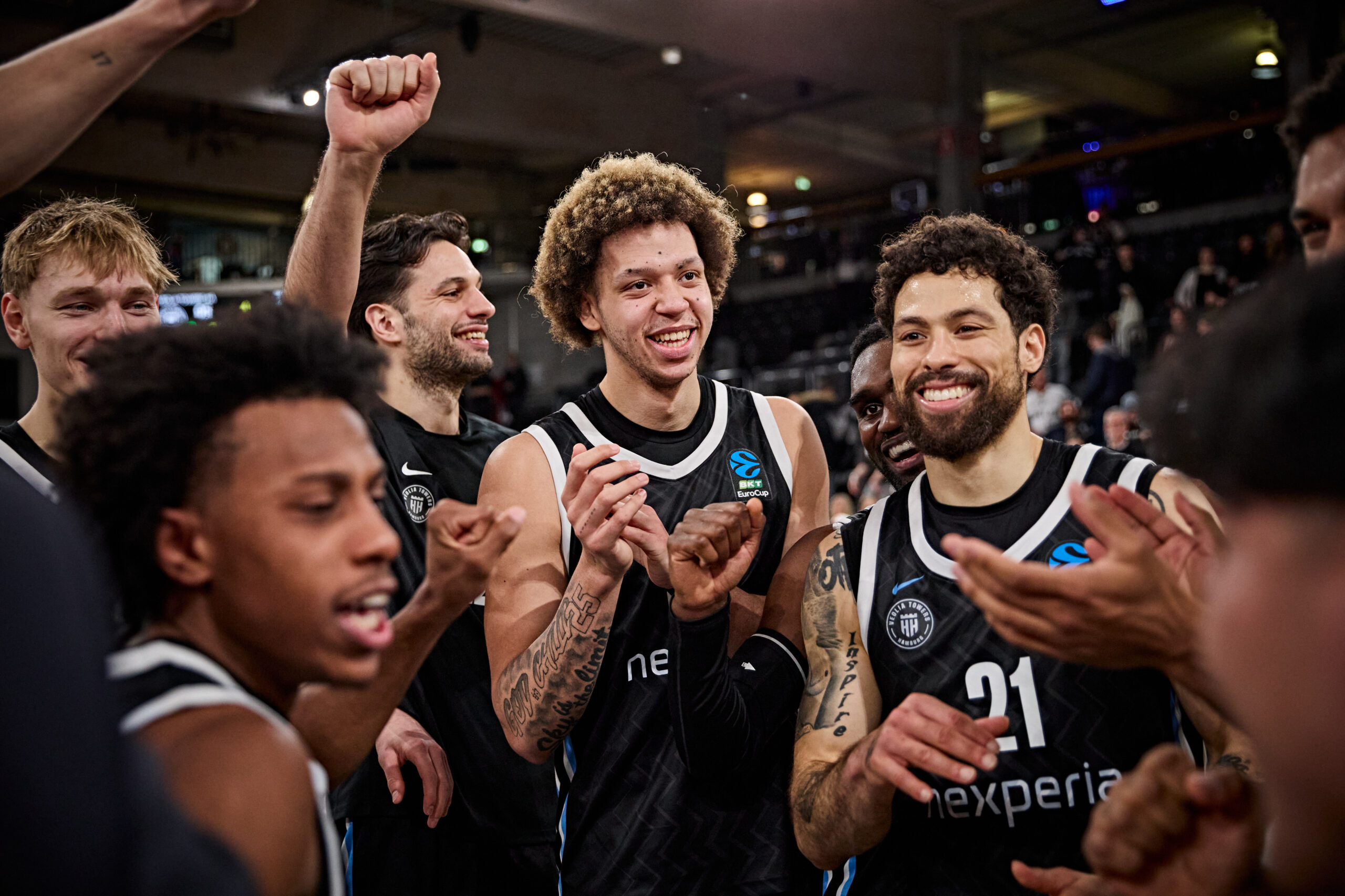 Basketballspieler in schwarzen Trikots mit weißen Details stehen im Kreis und klatschen sich ab