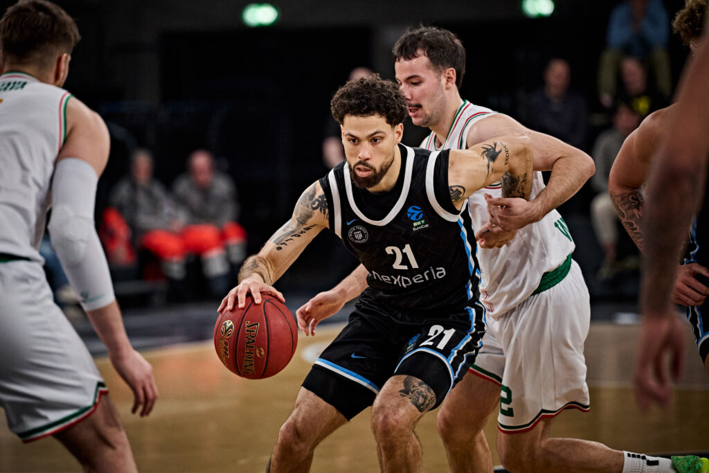Basketballspieler mit Trikot Nummer 21 dribbelt den Ball, umgeben von mehreren Gegenspielern in weißen Trikots.