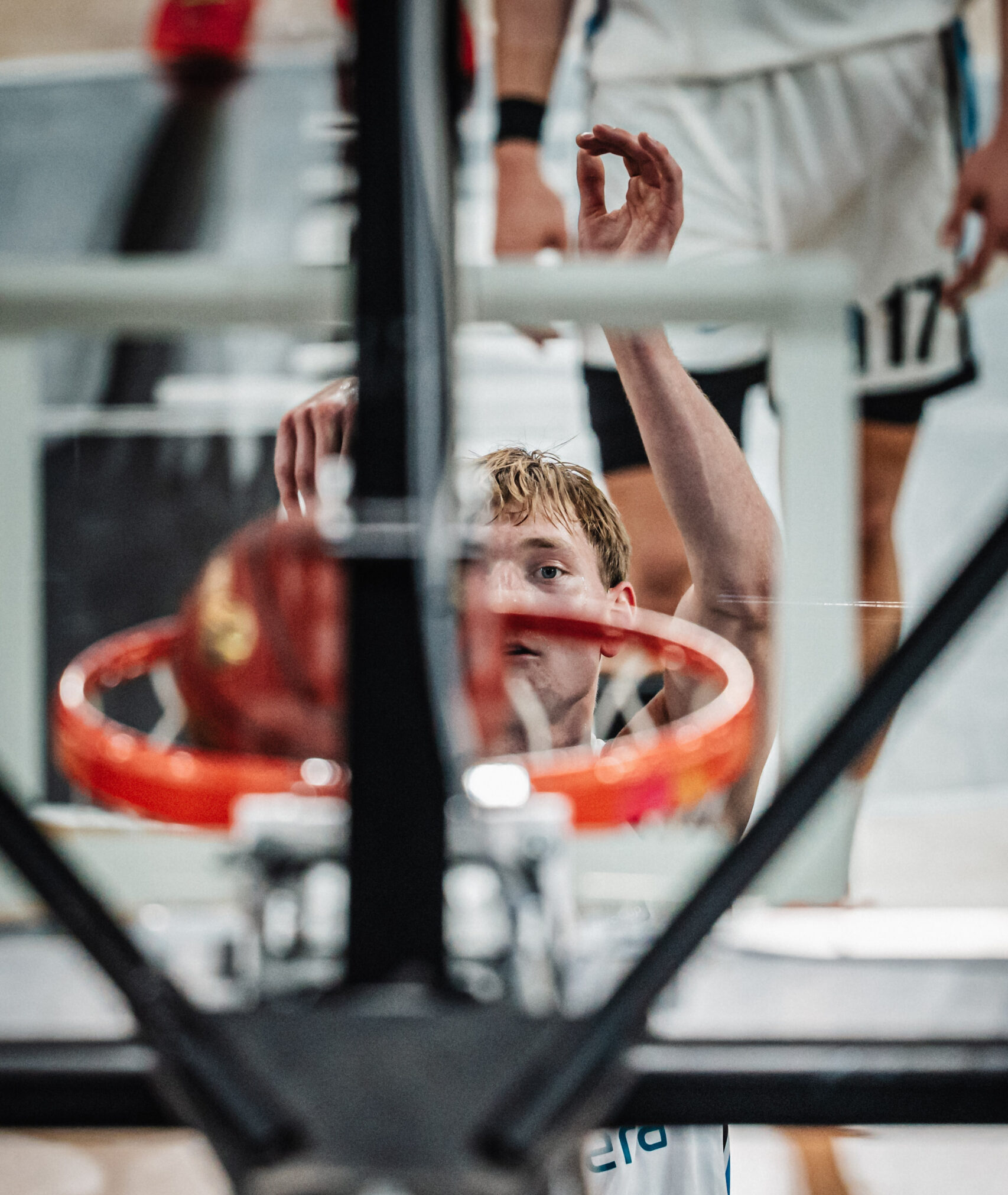 Ein Basketballspieler hebt den rechten Arm mit geformtem Ringfinger über dem Kopf, während er vor dem Basketballkorb steht.