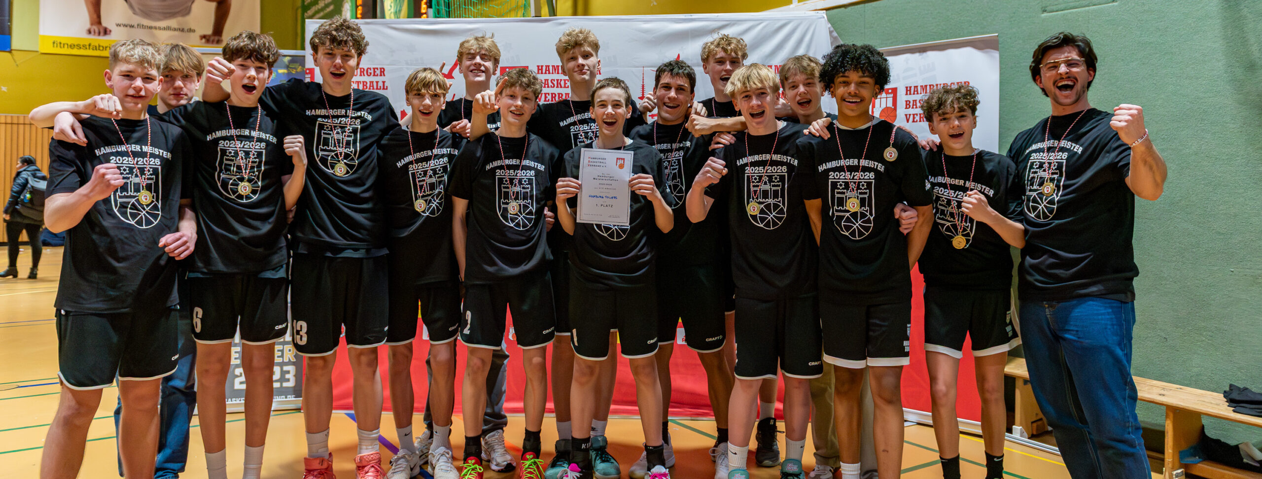 Gruppe von Jugendlichen in Sportkleidung mit Medaillen und Urkunde in einer Sporthalle
