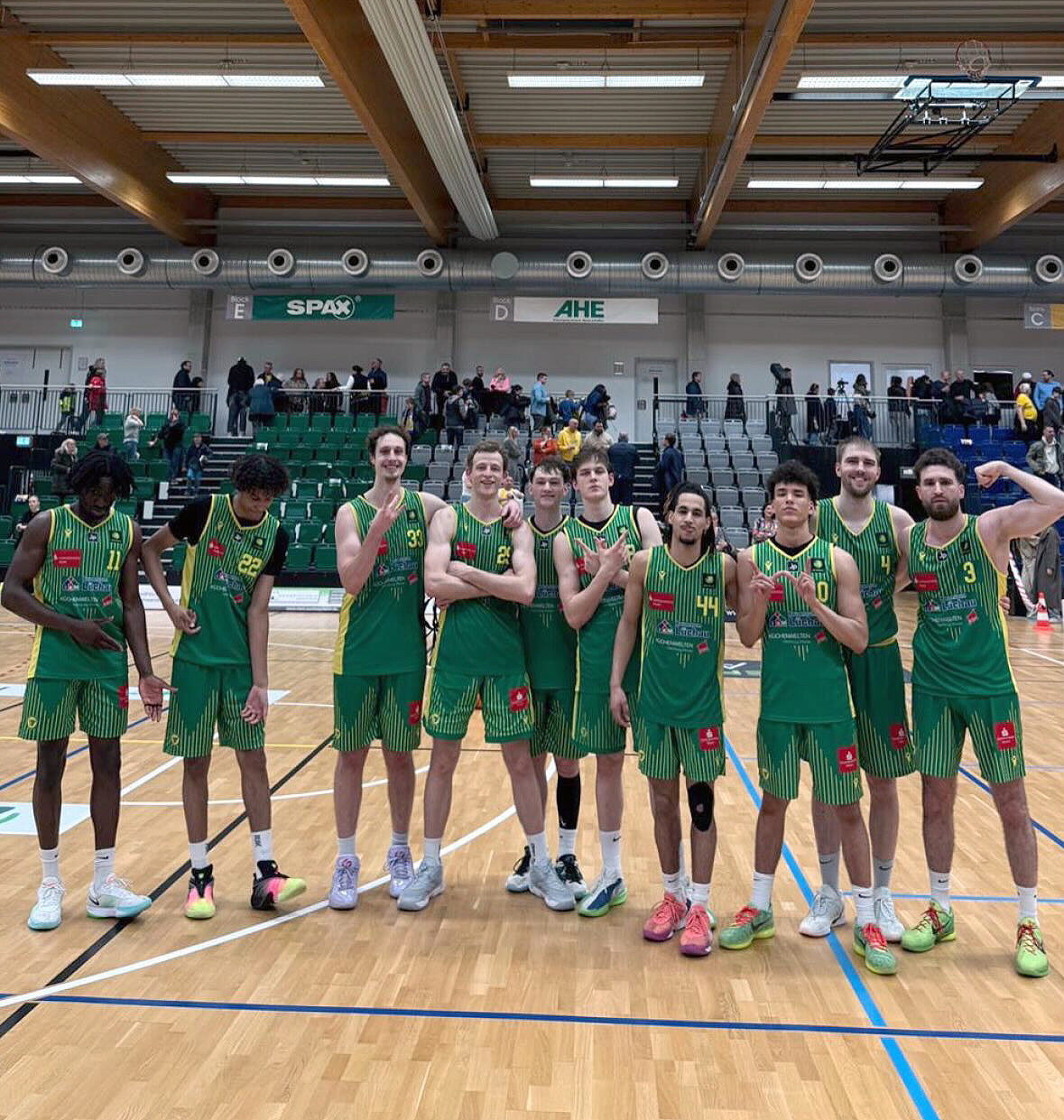 Gruppe von Basketballspielern in grünen Trikots steht in einer Sporthalle auf dem Spielfeld