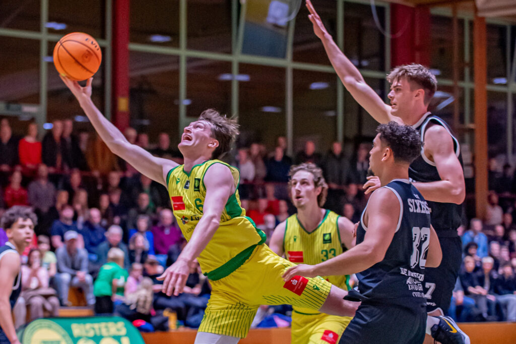 Basketballspieler in gelber Spielkleidung springen und versuchen, den Ball zu fangen, während Spieler in schwarzer Spielkleidung verteidigen