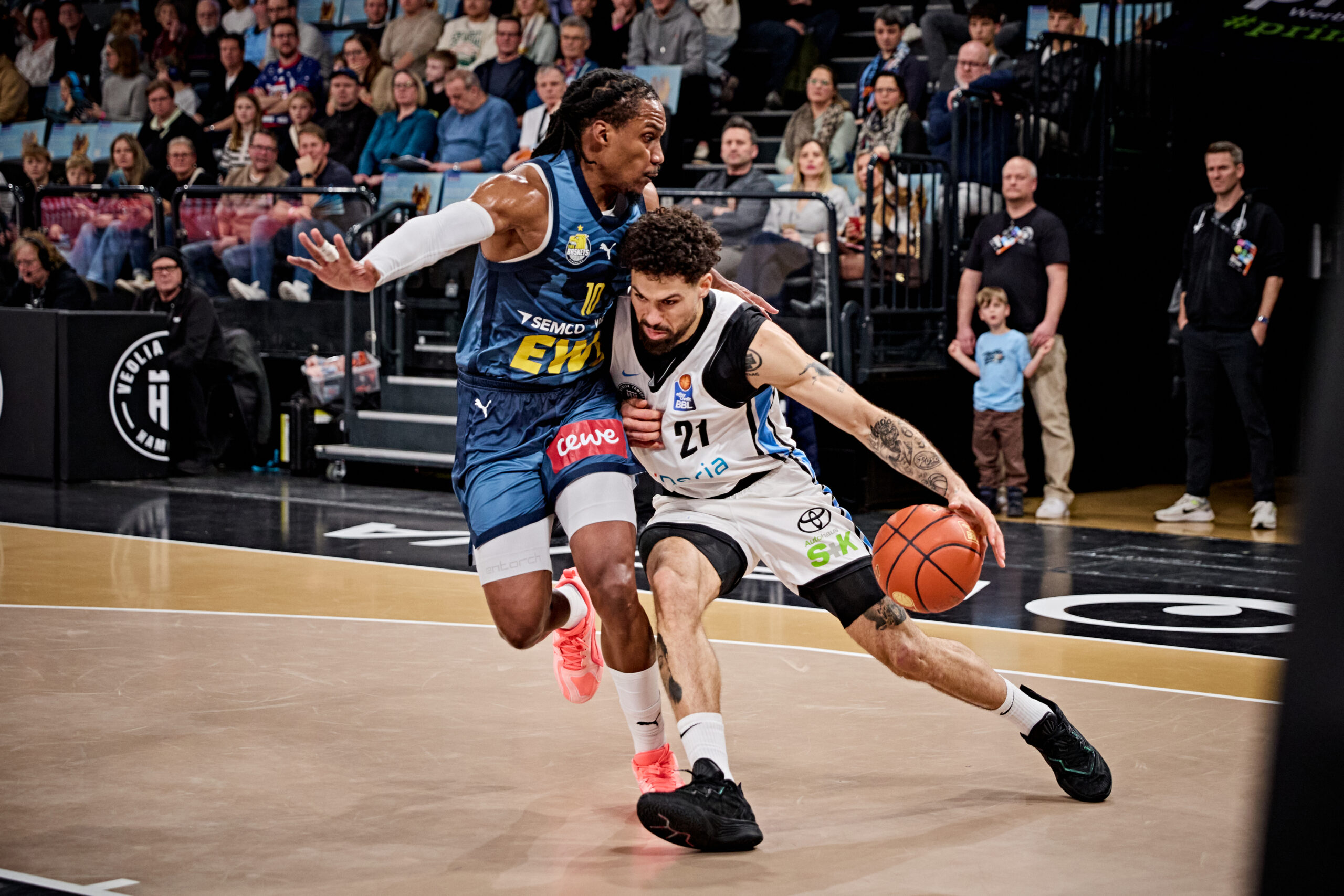 Zwei Basketballspieler in Aktion auf dem Spielfeld, einer dribbelt den Ball, der andere verteidigt.
