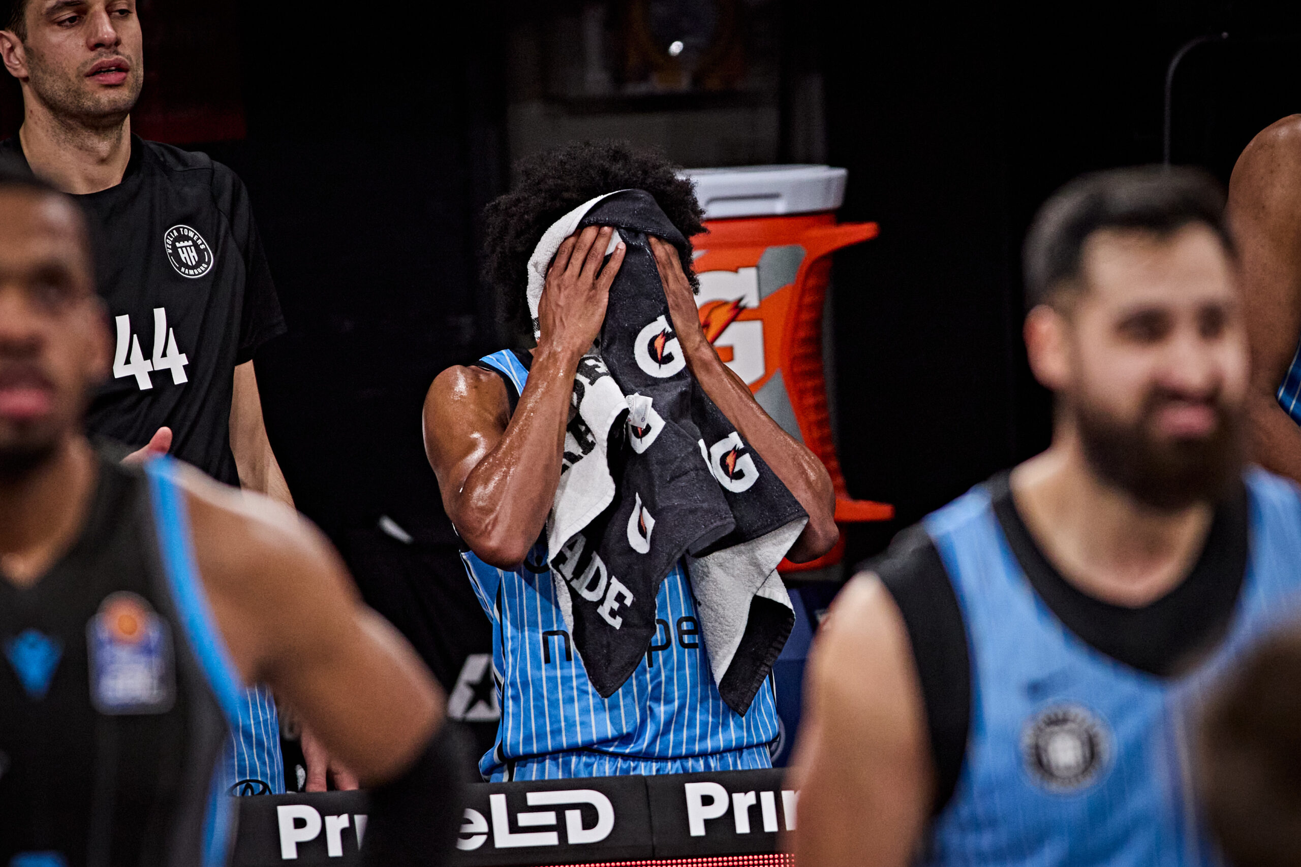 Basketballspieler in blauen Trikots stehen nebeneinander, einer hält sich ein Handtuch vor das Gesicht.