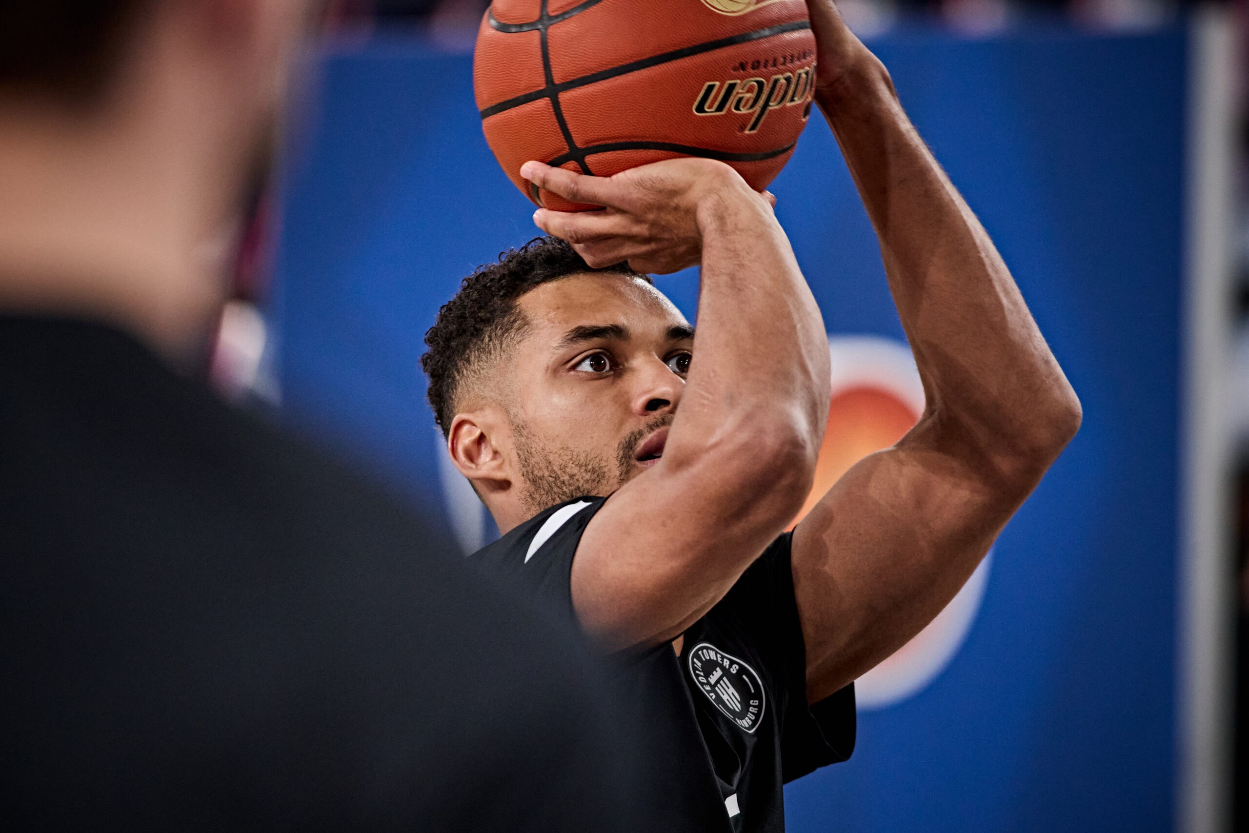 Basketballspieler in schwarzem Trikot mit Ball über dem Kopf in Wurfauslage