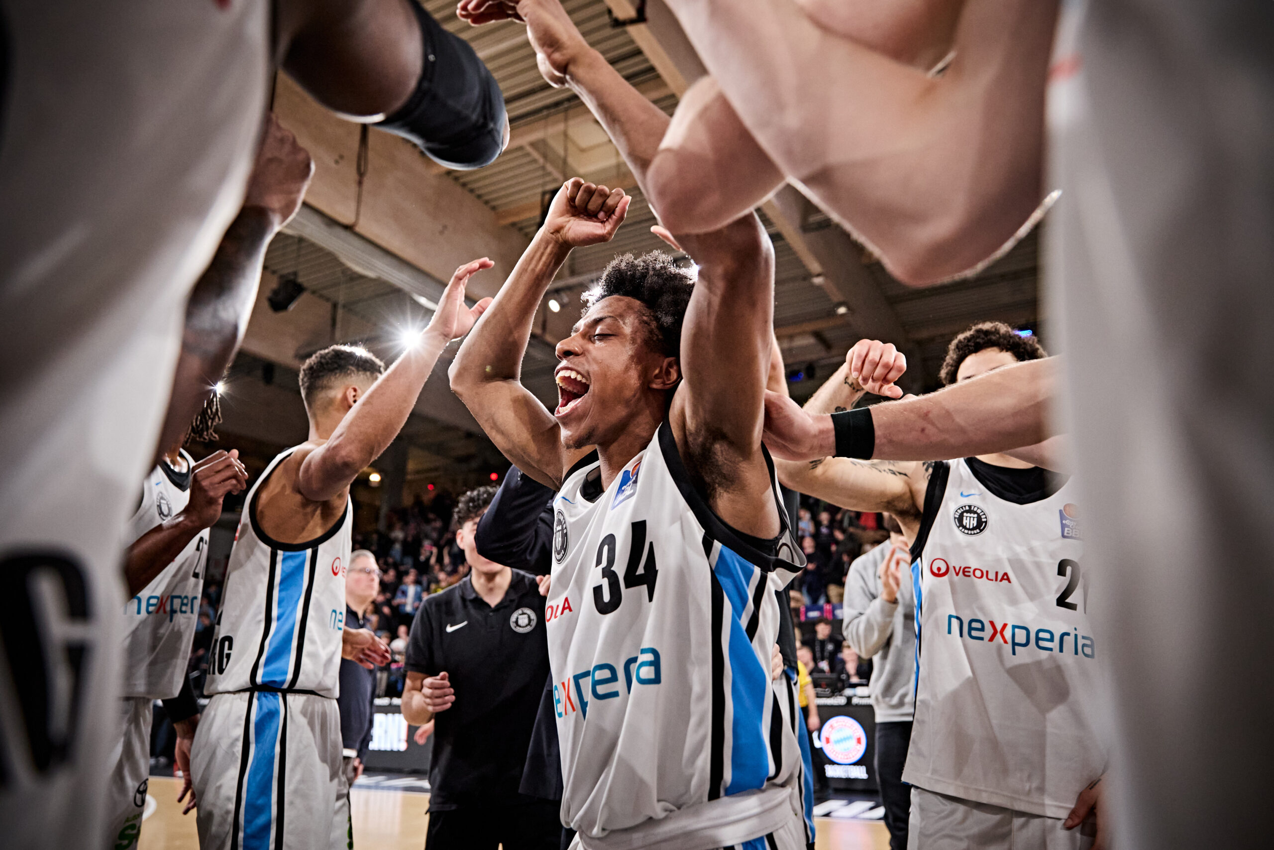 Basketballspieler in weißen Trikots mit erhobenen Armen in einer Teamrunde in der Halle