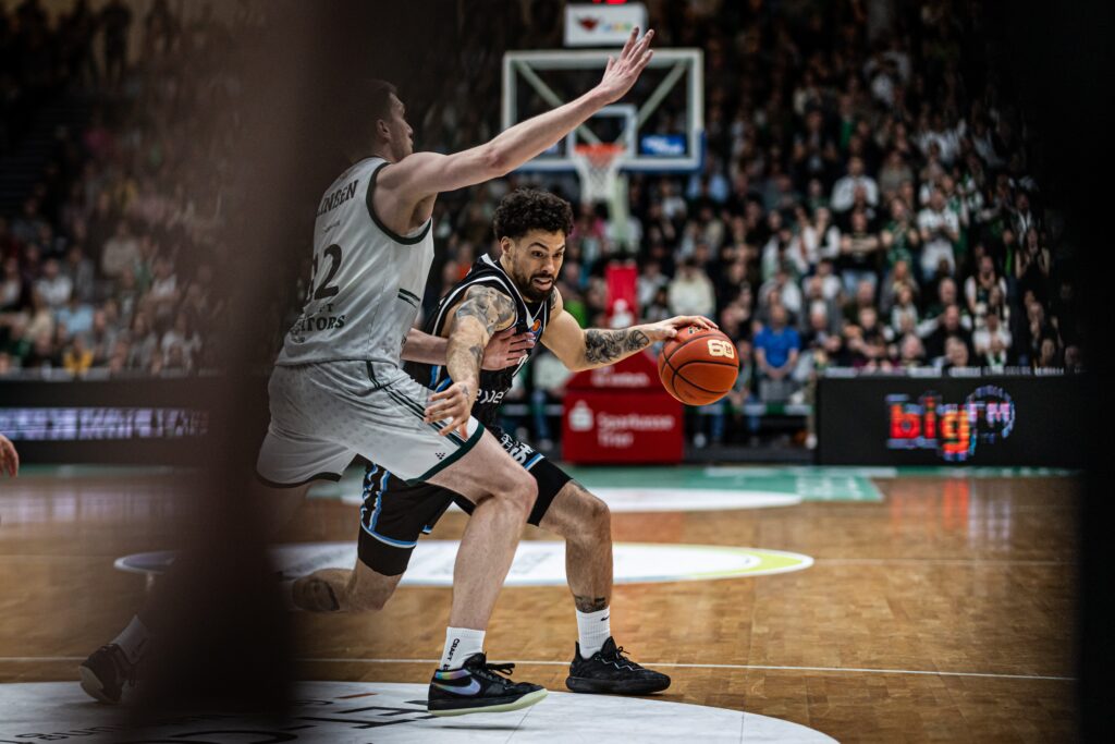 Zwei Basketballspieler in Aktion auf dem Spielfeld vor voller Zuschauerkulisse
