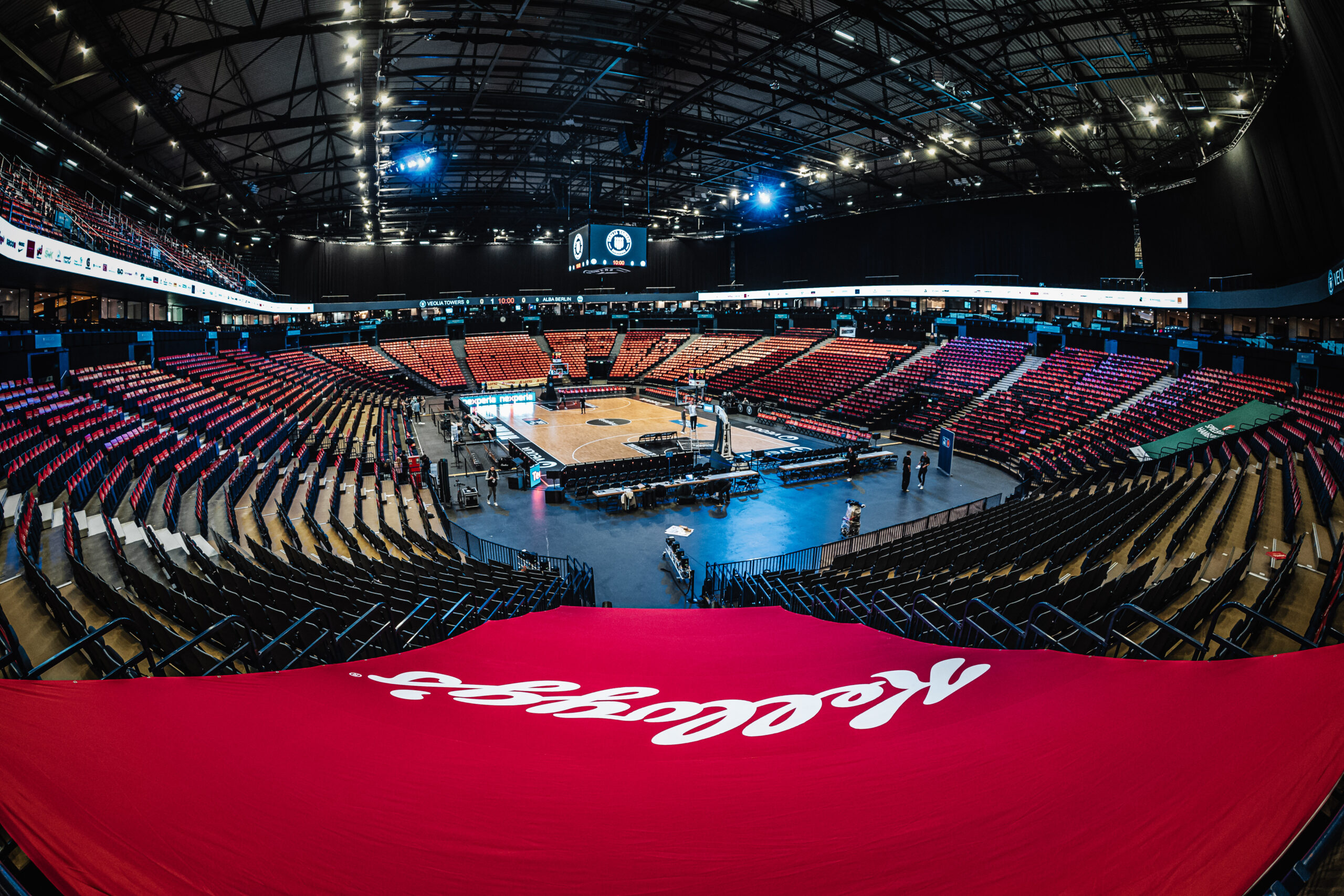 Leere Basketballarena mit Spielfeld in der Mitte und roten Sitzreihen