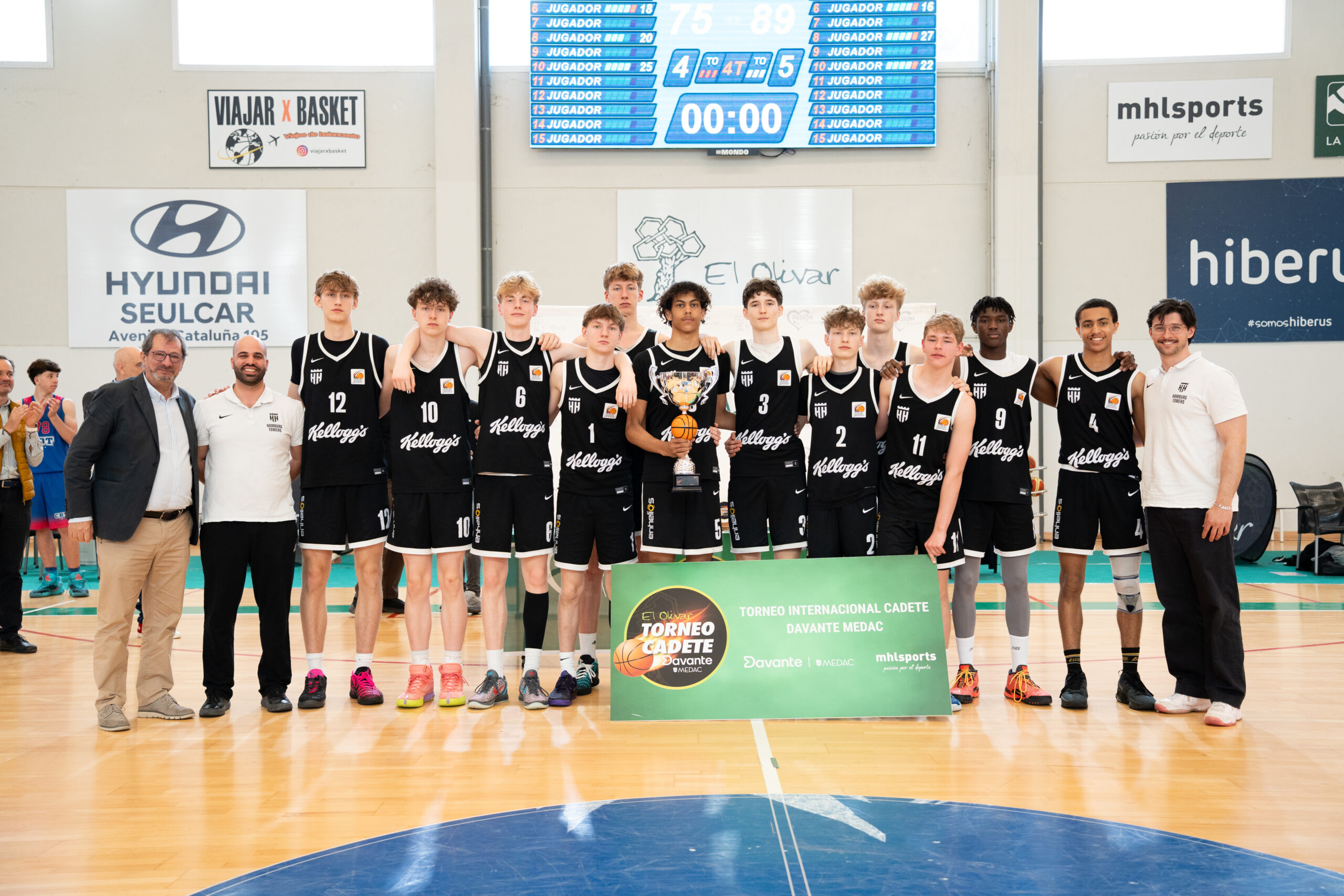 Jugend-Basketballmannschaft in schwarzen Trikots steht in einer Sporthalle nebeneinander mit einem Pokal und einem grünen Banner mit der Aufschrift 'TORNEO CADETE'
