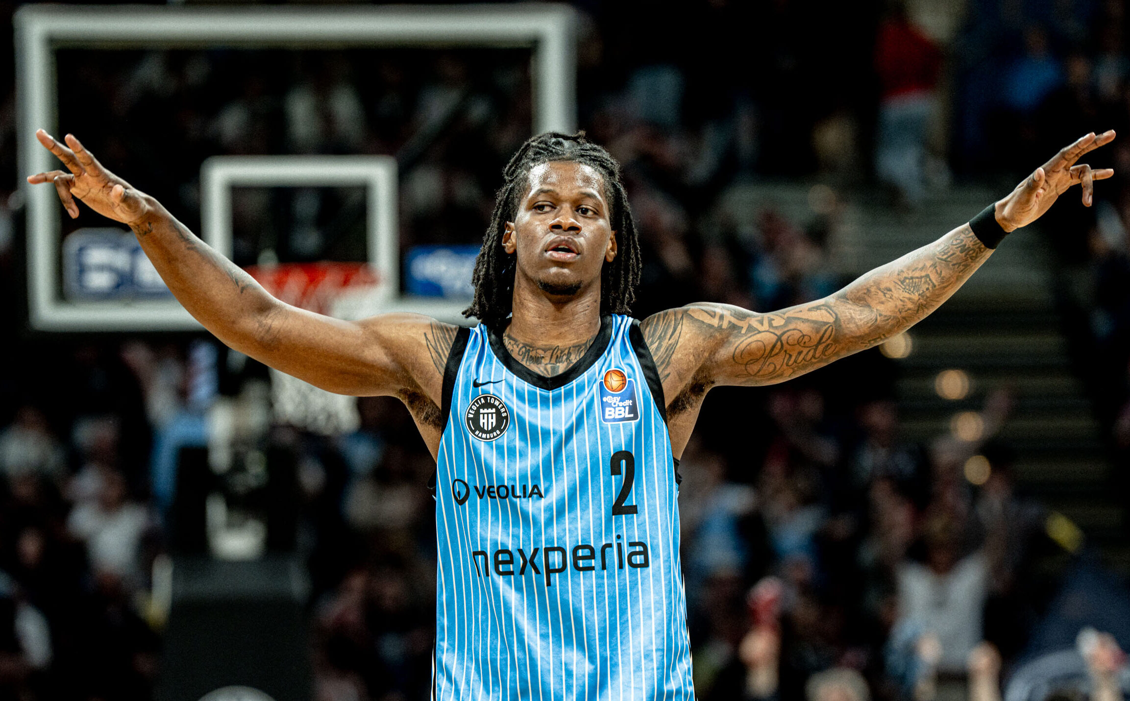 Basketballspieler mit hochgestreckten Armen in blau-weiß gestreiftem Trikot mit der Nummer 2 auf dem Spielfeld